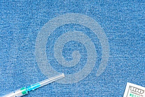Syringe and one hundred american dollars banknotes on a blue background. The background is denim