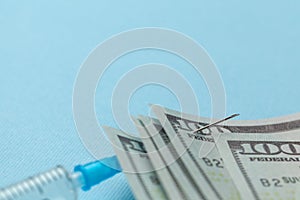 Syringe and paper dollars pinned to needle on blue background. Expensive medical insurance. Copy space for text.