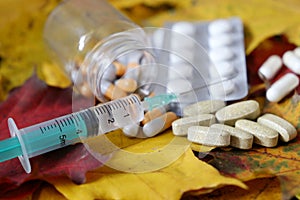 Syringe and pills on the autumn maple leaves