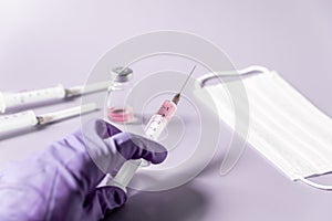 Syringe with a vaccine in hand in a medical glove on a purple background. Medical card, soft focus