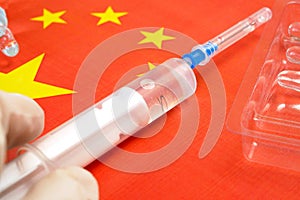 syringe with a vaccine is held by hand in a glove on background of the Chinese flag, vaccine against coronavirus