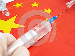 syringe with a vaccine is held by hand in a glove on background of the Chinese flag, vaccine against coronavirus,