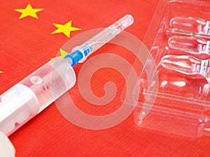 Syringe with a vaccine is held by hand in a glove on background of the Chinese flag, vaccine against coronavirus,