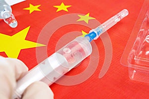 syringe with a vaccine is held by hand in a glove on background of the Chinese flag, vaccine against coronavirus