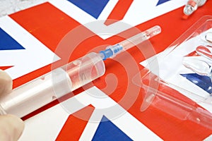 Syringe with a vaccine is held by  hand in a glove on background of the England flag, vaccine against coronavirus