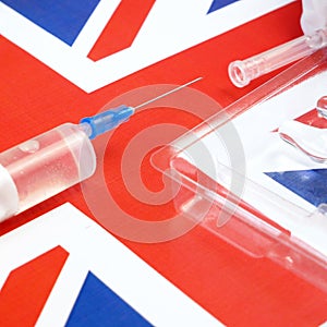 syringe with a vaccine is held by hand in a glove on background of the England flag, vaccine against coronavirus