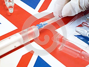 syringe with a vaccine is held by hand in a glove on background of the England flag, vaccine against coronavirus,