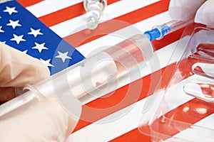 syringe with a vaccine is held by hand in a glove on background of the USA flag, vaccine against coronavirus