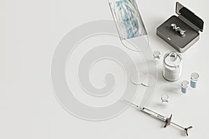 Syringe, vials, face mask on white background from above, coronavirus vaccination concept, medical supplies equipment on table,