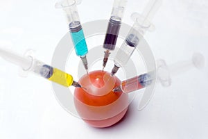 Syringes with green, red, yellow, black and white liquid make an injection into a red tomato on a white background. Concepts of