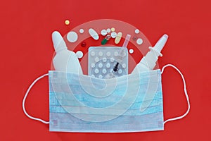 .syringes, pills and nasal sprays under a blue medical mask on a bright red background.