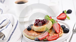 Syrniki with fresh berries, jam and cup of coffee