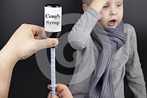 Syrup for sore throat for a child. The medicine in a syringe on the background of a sick boy. The concept of treating children at