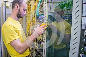 The system administrator is testing the network with a reflectometer.  The man works in the server room of the datacenter. A