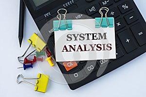 SYSTEM ANALYSIS - words on a white sheet with clips on a white background with a calculator, buttons and yellow stationery clips