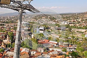 System of cableway and vmoving cabin over city of old buildings and historical area of georgian capital