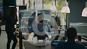 System engineer checking code on multiple monitors and working with app developer