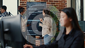 System engineers comparing source code on wall screen tv analyzing errors using digital tablet