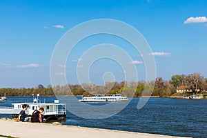 Tourist boat on Szentendre branch of Danube River on sunny day. Family resting on the shore. Space for text