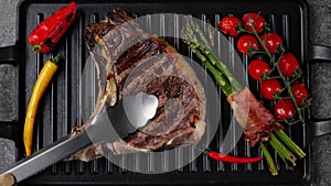 T- bone beef steak grill with vegetables on grill pan. Steak turning over on the grill. Top view. Slow motion