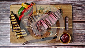 T- bone beef steak grilled sliced with grilled vegetables on wooden board. Top view