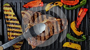 T- bone beef steak turn over on grill, with grilled vegetables. Slow motion. Top view