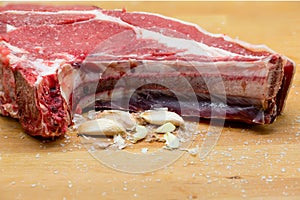 T-bone steak with garlic cloves and coarse salt on a wooden board. Veal. tender garlic photo