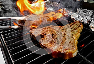 T-bone steak grilled on a hot and smoky oven sprinkled  rosemary with side dishes wrapped in foil and grilled.