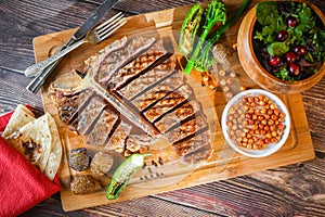 T-bone steak grilled in pieces on wood with hot pepper and salad