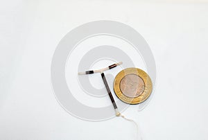 T shape IUD Gold hormon free birth control device beside a coin for size and shape realisation on white background. Selective