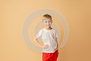 T-shirt design concept - smiling little boy in blank white t-shirt on a beige background