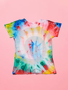 T-shirt painted in tie dye style on a pink background. Flat lay. Pastel color.