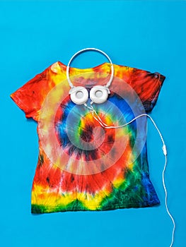 T-shirt with a spiral tie dye pattern and headphones on a blue background. Flat lay. Pastel color.