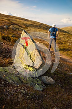 T sign on rock and hiker with backpack traveling in Norway mount