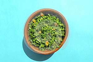 Tabbouleh green salad in a brow on bright blue background. Top view.