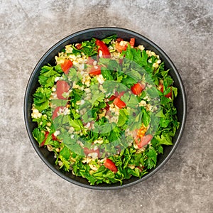 Tabbouleh salad with bulgur, parsley, spring onion and tomato in bowl on grey background. Top view