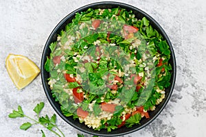 Tabbouleh salad with bulgur, parsley, spring onion and tomato in bowl on grey background. Top view