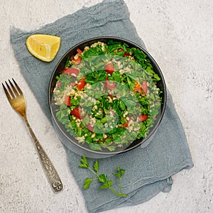 Tabbouleh salad with bulgur, parsley, spring onion and tomato in bowl on grey background. Top view