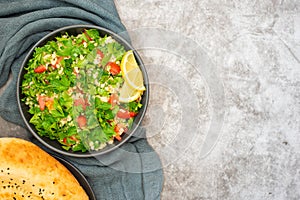 Tabbouleh salad with bulgur, parsley, spring onion and tomato in bowl on grey background. Top view. WIth copy space