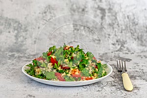 Tabbouleh salad with bulgur, parsley, spring onion and tomato in bowl on grey background. Top view. WIth copy space