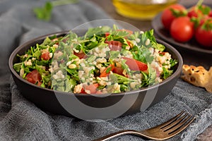 Tabbouleh salad with bulgur, parsley, spring onion and tomato in bowl on grey background. Top view. WIth copy space