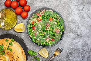 Tabbouleh salad with bulgur, parsley, spring onion and tomato in bowl on grey background. Top view. WIth copy space