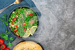 Tabbouleh salad with bulgur, parsley, spring onion and tomato in bowl on grey background. Top view. WIth copy space