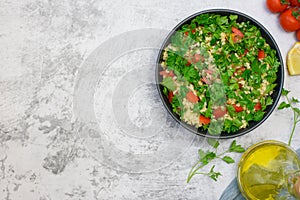 Tabbouleh salad with bulgur, parsley, spring onion and tomato in bowl on grey background. Top view. Copy space