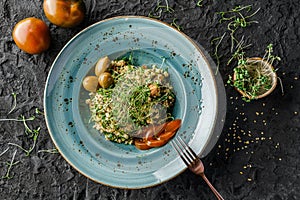 Tabbouleh salad with bulgur, seedlings, tomatoes and olives in plate on dark background.