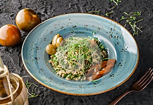 Tabbouleh salad with bulgur, seedlings, tomatoes and olives in plate on dark background. Healthy vegan food, clean eating, dieting