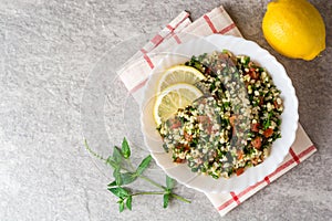 Tabbouleh salad with bulgur, tomatoes, parsley, green onion and mint in plate on grey stone table.