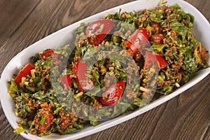 Tabbouleh salad with bulgur, tomatoes, parsley and green onion in plate on wooden table