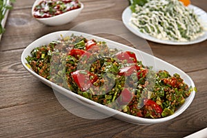 Tabbouleh salad with bulgur, tomatoes, parsley and green onion in plate on wooden table.