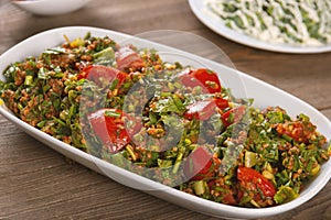 Tabbouleh salad with bulgur, tomatoes, parsley and green onion in plate on wooden table.